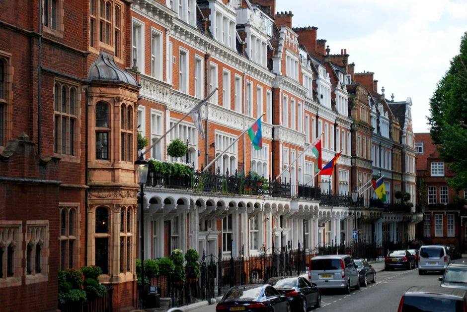 Old house of embassy with flags located in modern street full of cars and bushes