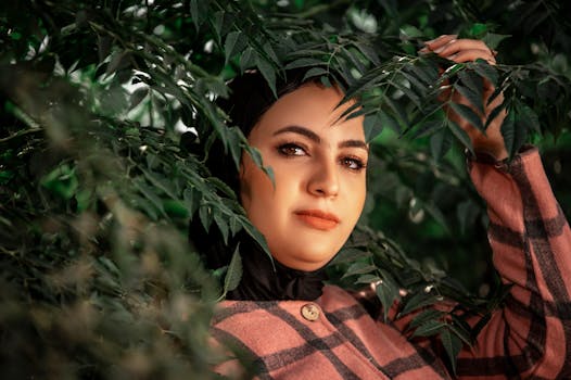 Portrait of a woman in a pink checkered coat surrounded by lush green leaves.