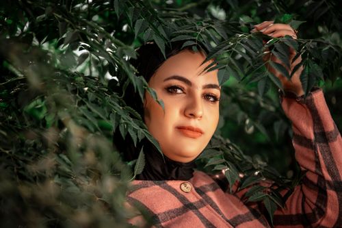 Free Portrait of a woman in a pink checkered coat surrounded by lush green leaves. Stock Photo