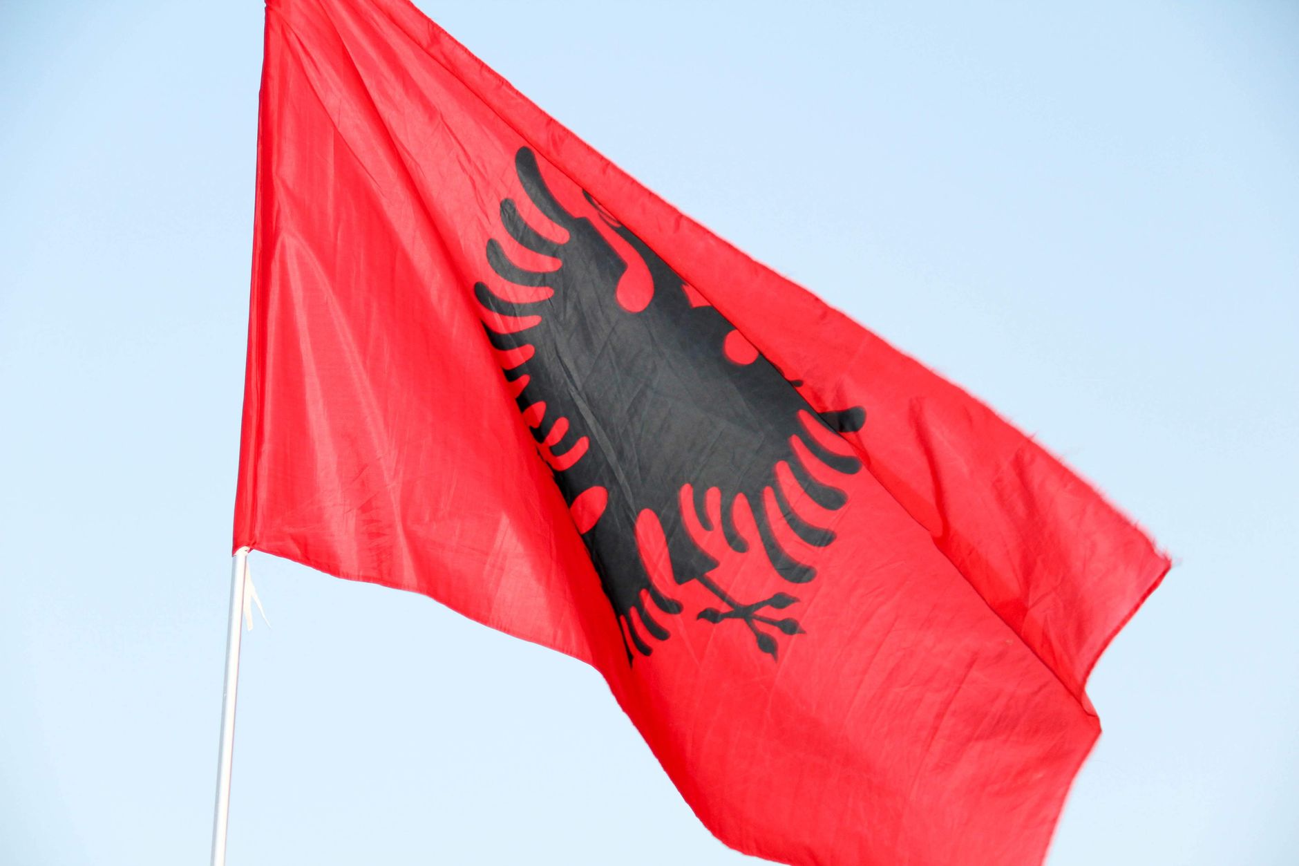 A vibrant red flag with a black double-headed eagle, symbolizing Albania, waving proudly against a clear blue sky.