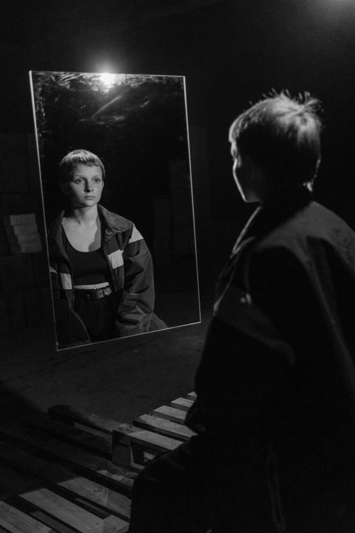 Free A young adult woman looks at her reflection in a mirror, captured in black and white. Stock Photo
