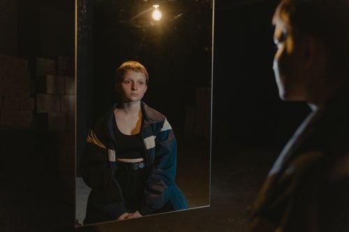 Free A young woman reflecting in a mirror under soft light, evoking introspection and serenity. Stock Photo