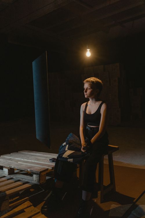 Free Moody portrait of a woman in a dimly lit industrial space, contemplating under a single light bulb. Stock Photo