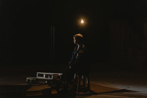 A Woman Witting on the Chair Under the Lightbulb Near the Wood Pallet