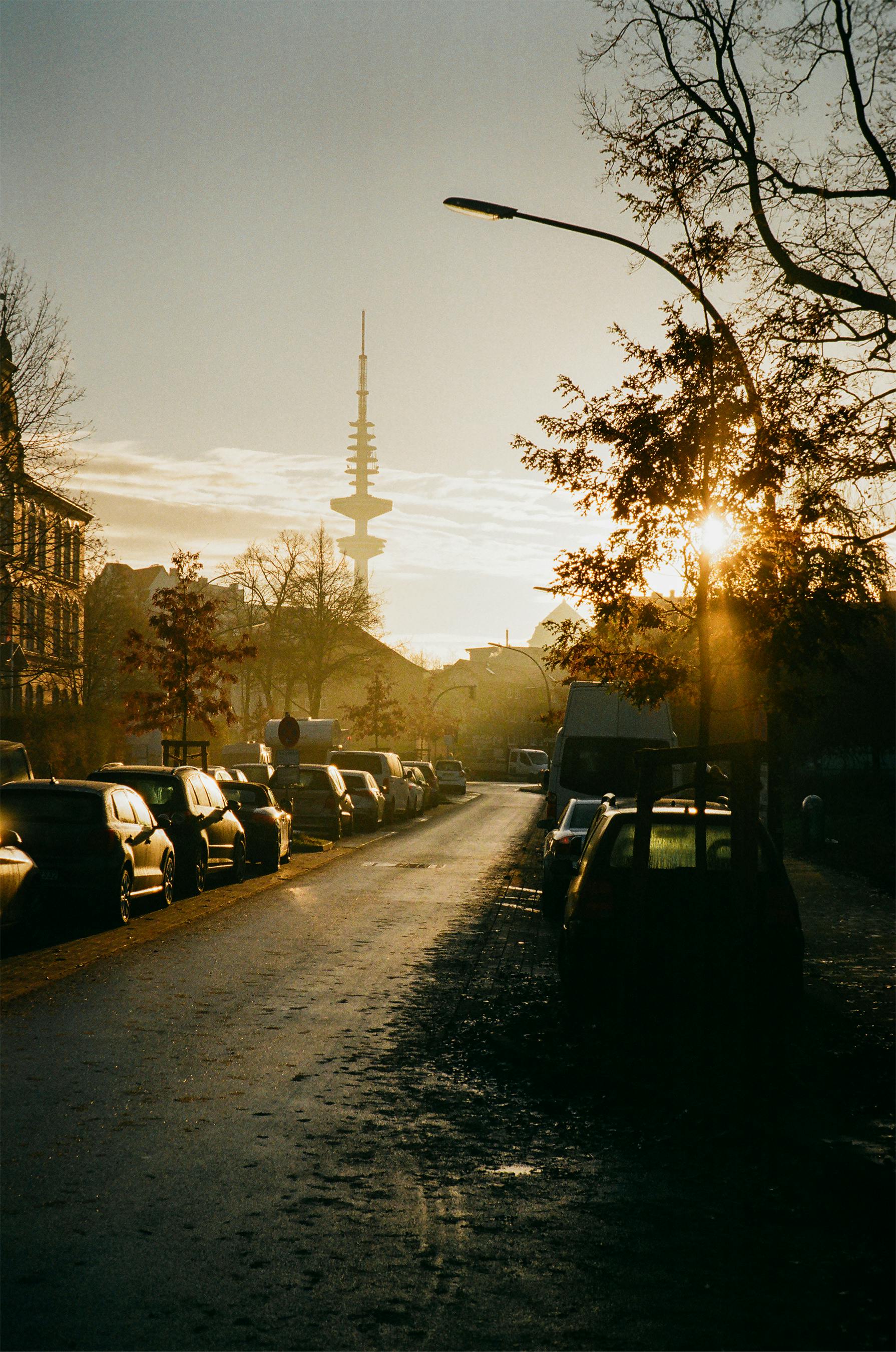 A tranquil street in Hamburg during sunset with the iconic telecommunication tower in the background.