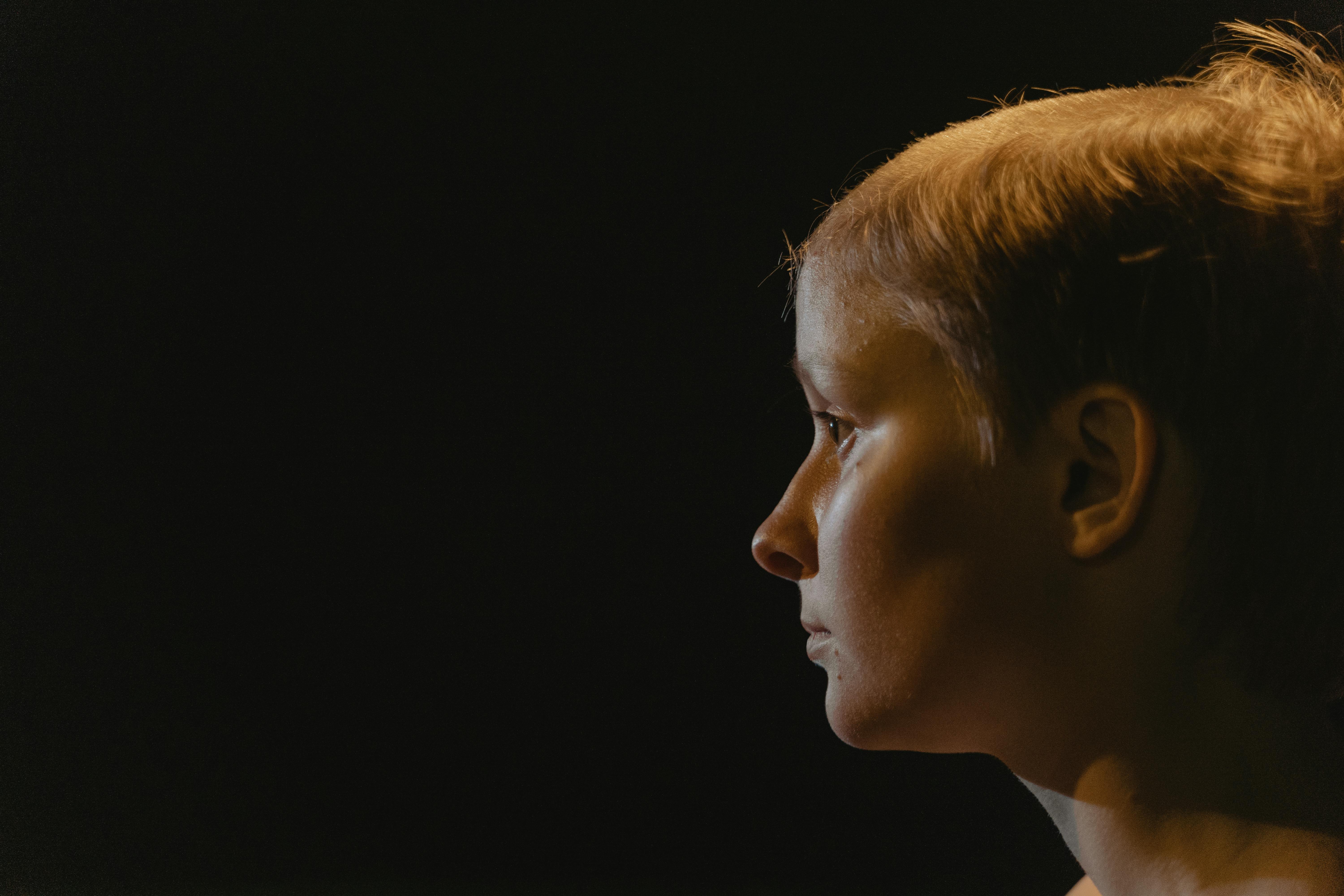 A close-up side profile of a woman with short hair, captured in dramatic lighting, emphasizing her features.