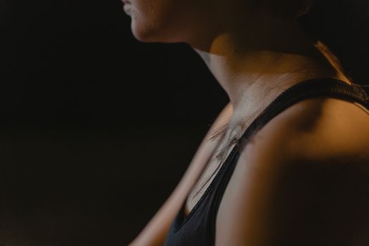 Close-up of a woman's neck wearing a tank top in low light, creating a moody atmosphere.