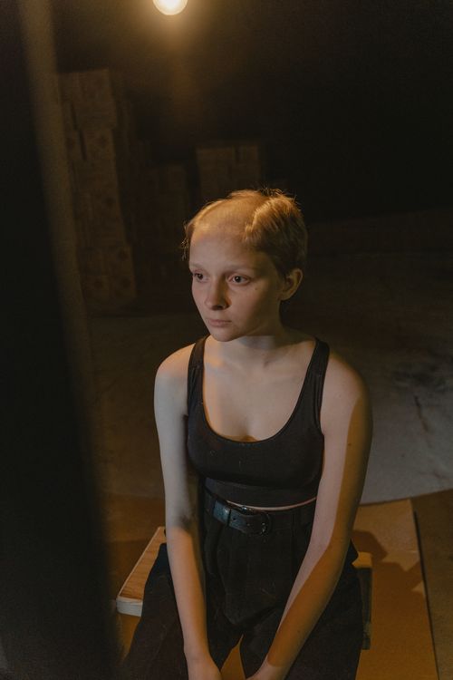 Free A woman with a shaved head sitting indoors under moody lighting, creating a thoughtful ambiance. Stock Photo