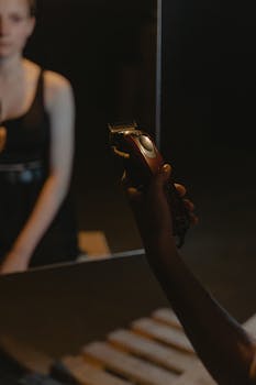 A person holding an electric shaver in front of a mirror with another individual visible in the reflection.