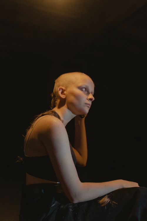 Free Portrait of a bald woman sitting in dim light, exuding a contemplative and mysterious mood. Stock Photo