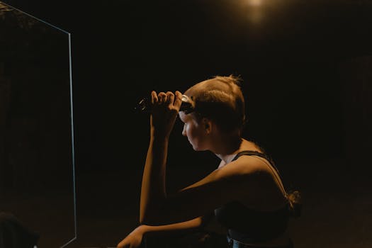 A young woman shaves her head in a dimly lit room, symbolizing change and empowerment.