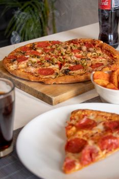 Appetizing pepperoni pizza on a cutting board with a refreshing drink and potato wedges nearby.