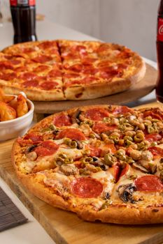 Appetizing pepperoni pizzas with mixed toppings and drinks on a table.