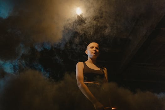 Bald woman in black tank top surrounded by smoke and dramatic lighting.
