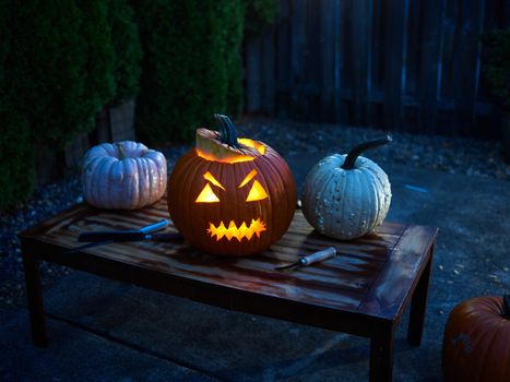 A glowing carved pumpkin Jack-o'-Lantern sits on a wooden table, creating a spooky Halloween scene.
