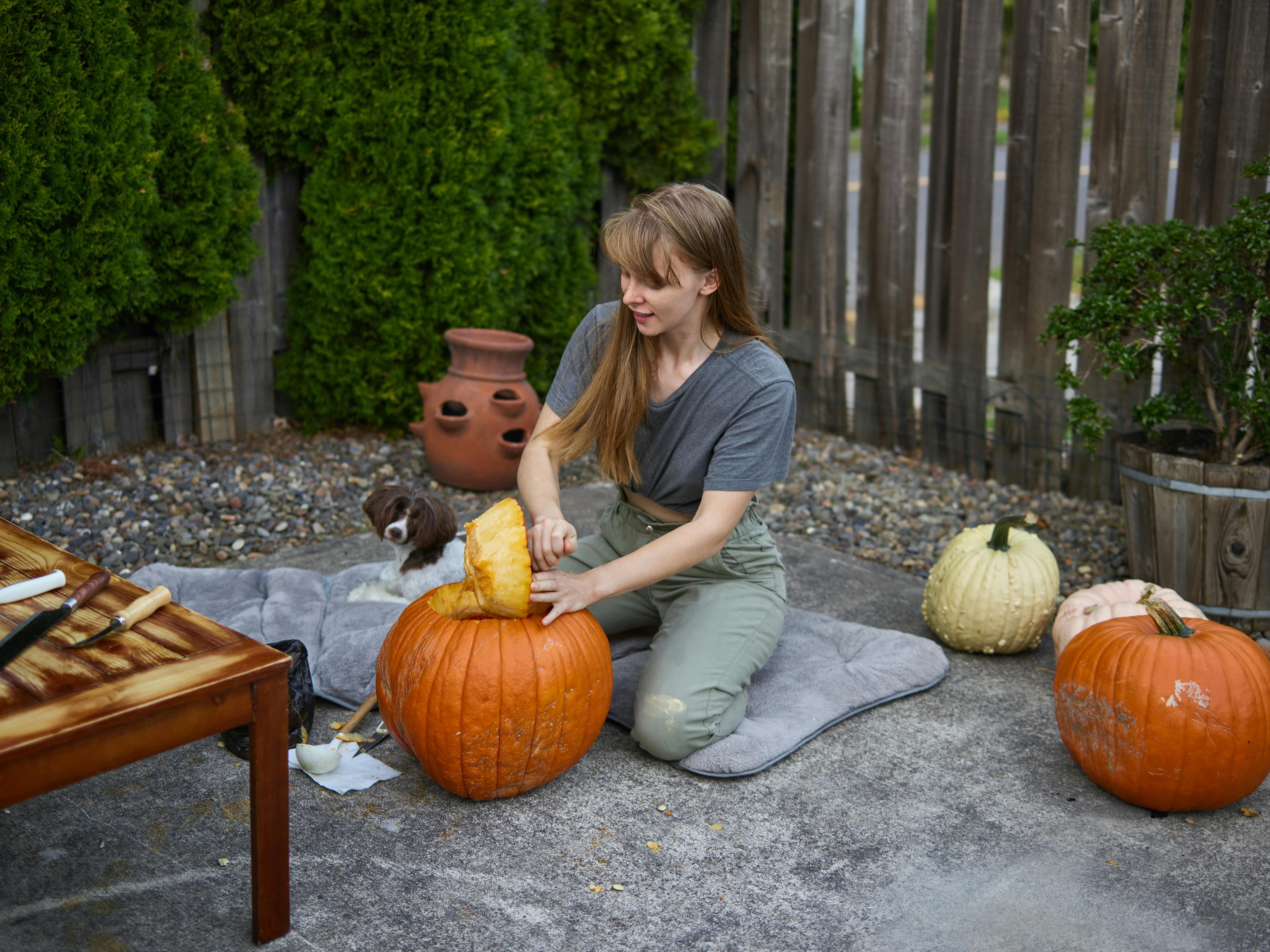 woman sitting on ground while carving pumpkin