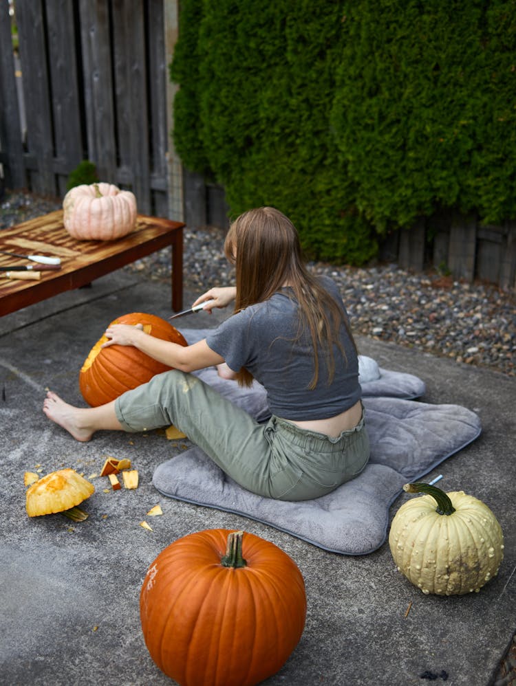 A Woman Carving A Pumpkin While Sitting On The Ground