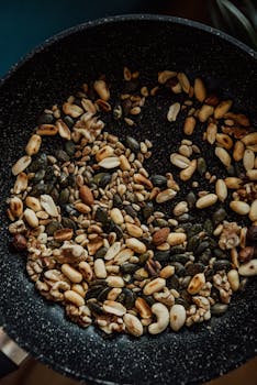 Close-up of assorted nuts and seeds roasting in a frying pan, ideal for vegan cooking.