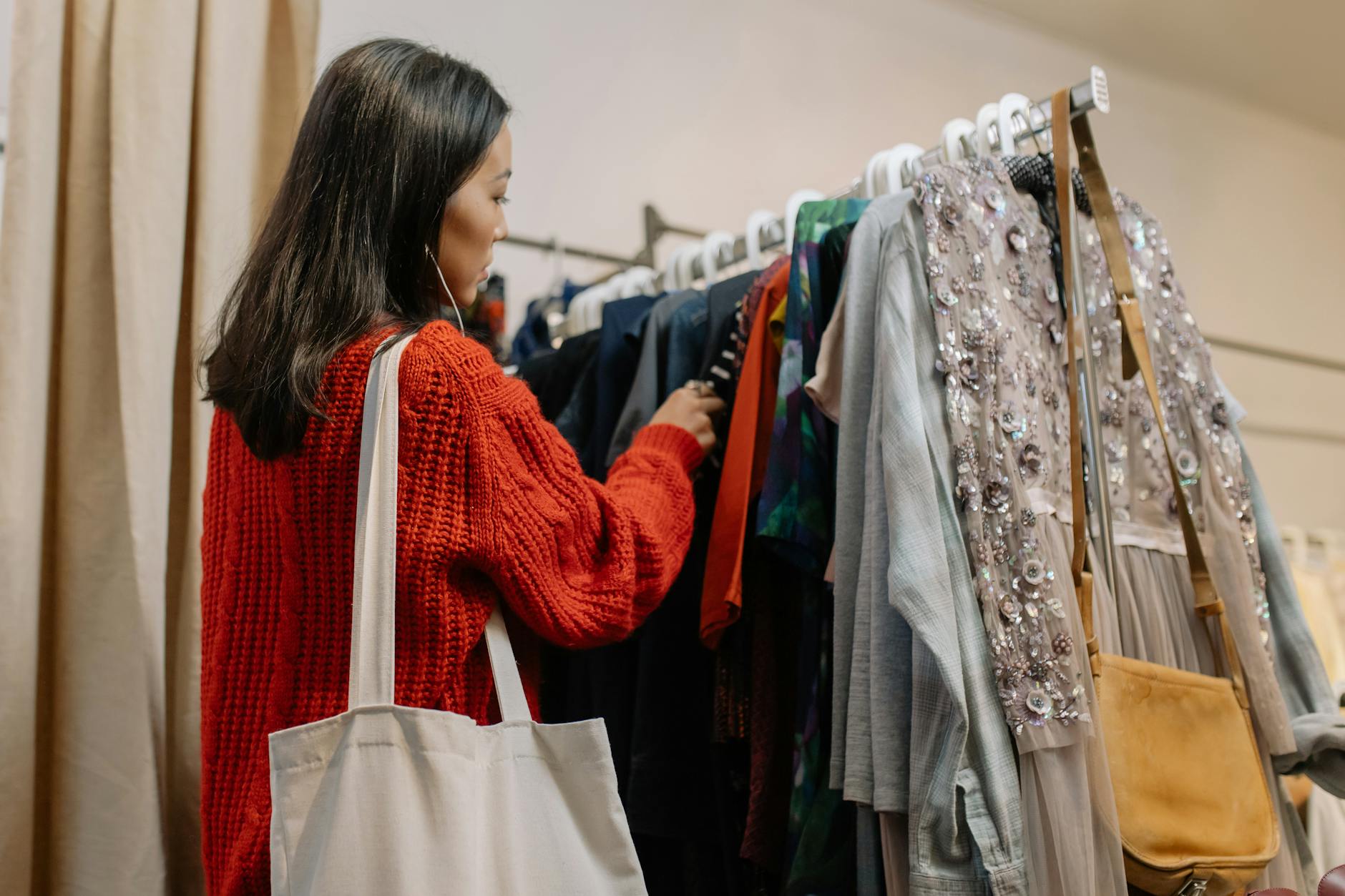 A woman in a red sweater is looking at clothes on a rack. 
Photo by cottonbro on Pexels