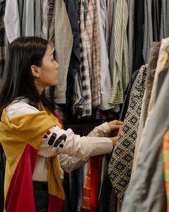 A young woman browsing clothes in a vintage store with colorful outfits.