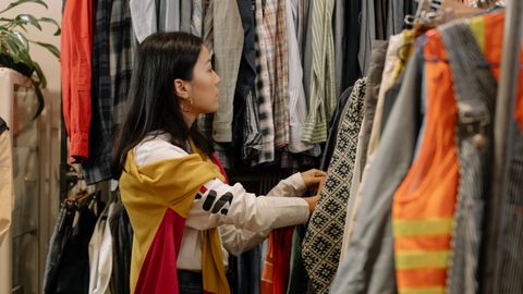 A young woman browsing clothes in a vintage store with colorful outfits.