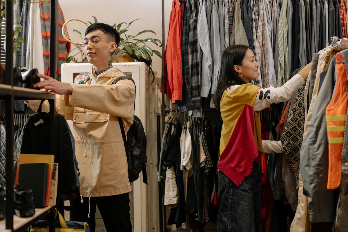 Dua anak muda thrifting di rak pakaian bekas berkualitas dengan koleksi vintage lengkap