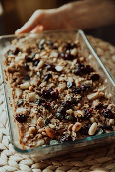 Close-up of a homemade granola bar in a glass tray, showing mixed nuts and dried fruits.