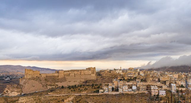 Dramatic clouds over an ancient fortress and cityscape in a desert environment.
