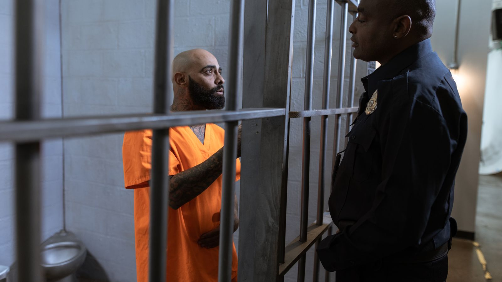 A guard converses with an inmate inside a prison cell, highlighting the justice system setting.
