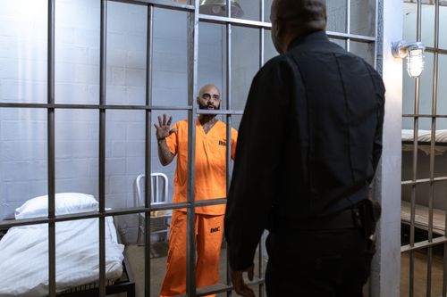 Free A male prisoner in an orange uniform stands behind bars facing a guard in a jail cell. Stock Photo