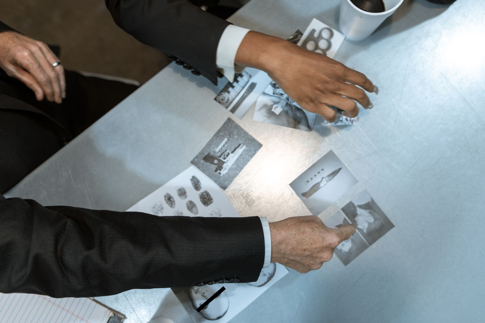 Detectives analyzing photographs and fingerprint records spread across a table