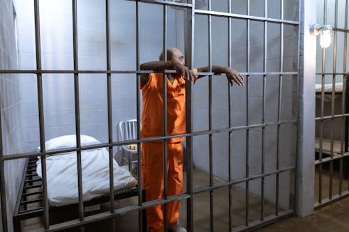 Man in Orange Uniform Standing Beside Gray Metal Gate