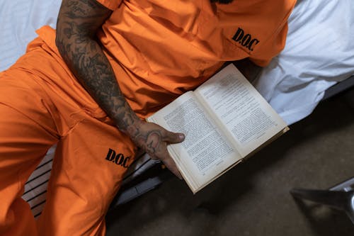 Person in Orange Shirt with Tattooed Arm Reading Book