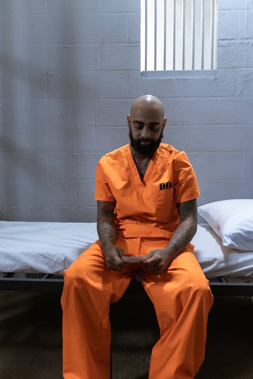 Free Man in Orange Clothes Sitting on the White Bed Stock Photo