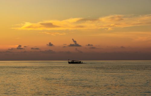 Free A silhouette of a boat gliding on calm sea during a stunning sunset. Stock Photo