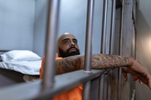 Man in Orange Shirt Standing beside Gray Metal Bars