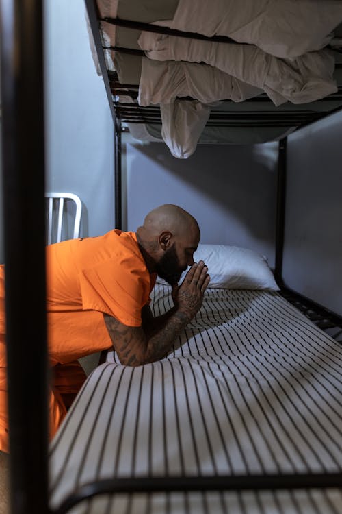 Man in Orange Polo Shirt Praying on the Bed