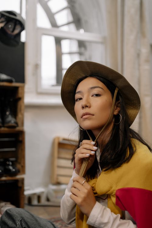 Free Young woman wearing a stylish hat and casual attire in an indoor setting, exuding confidence and modern flair. Stock Photo