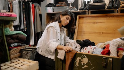 Young woman browsing vintage garments in a cozy thrift shop setting.