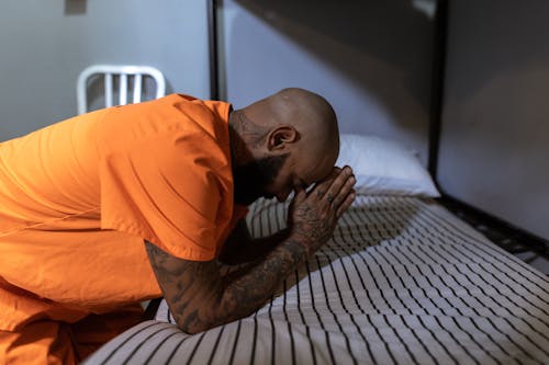 Free Man in Orange T-shirt Praying on Bed Stock Photo