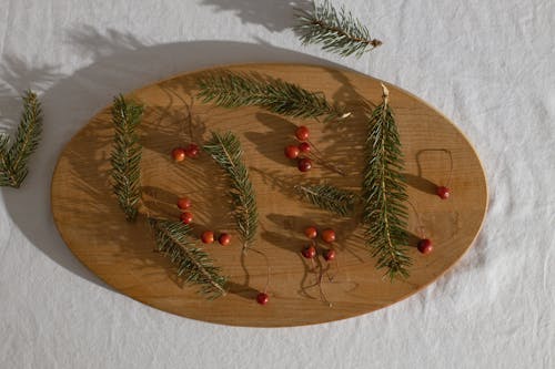 Top view of green coniferous branches near red ripe fresh holly berries on wooden board in daylight