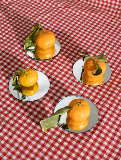 From above of ripe shiny tangerines with green leaves placed on cardboard cake base on red checkered tablecloth