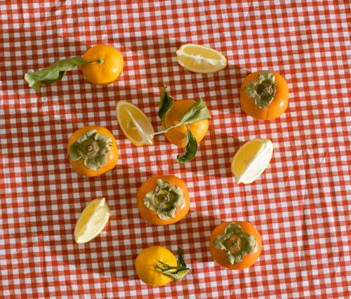 Free Top view of healthy food of lemon persimmon and tangerine placed on red checkered tablecloth Stock Photo