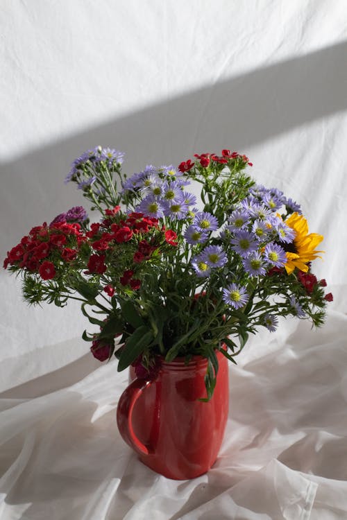 Bouquet of fresh wildflowers placed in ceramic red vase on white background in light room at floor