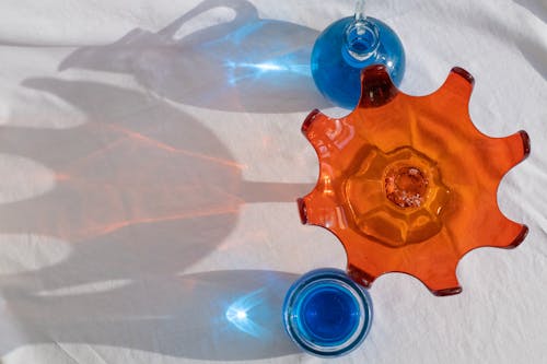 Top view of unusual orange bowl with glass bottles filled with blue liquid arranged on white textile