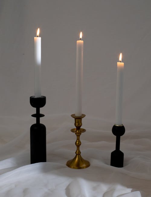Row of composed elegant candlesticks with burning white candles on white textile in studio