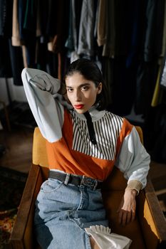 Portrait of a stylish woman in a retro outfit sitting in an indoor setting, exuding elegance.