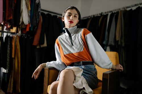 Free Confident woman in a stylish retro outfit posing on a chair. Vintage fashion in a modern setting. Stock Photo