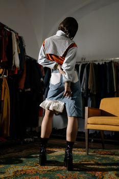 Back view of a stylish woman in a denim skirt and black boots, standing indoors.