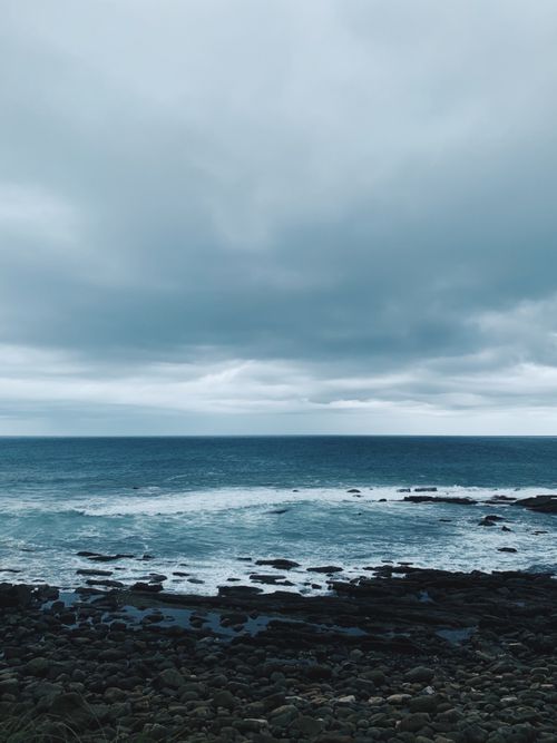 Free A captivating view of the ocean with dramatic clouds and a rocky shoreline. Stock Photo